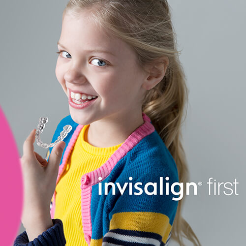 A little girl smiling while holding her Invisalign® aligners